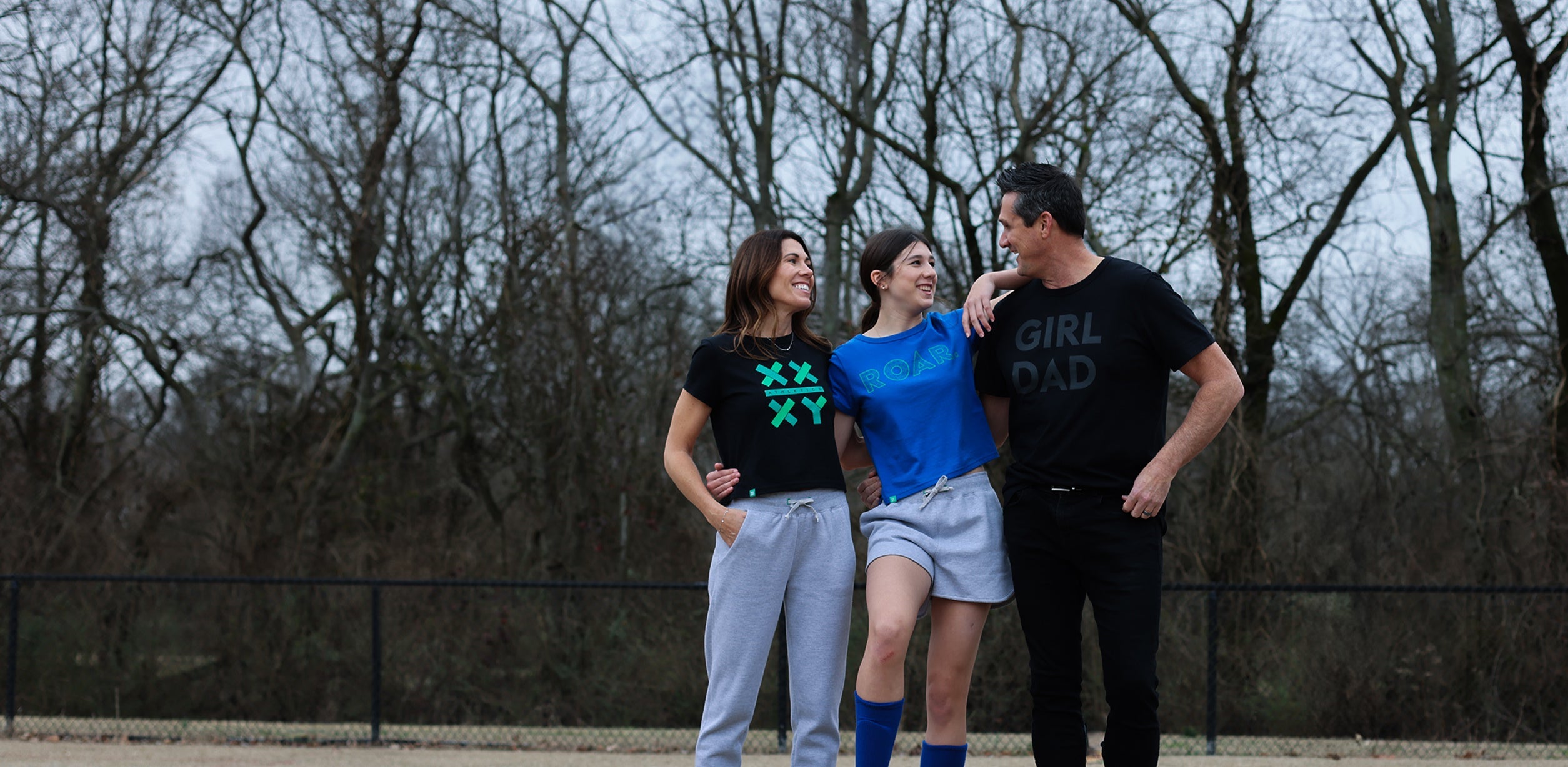 A man and two women standing next to each other wearing various XX-XY Athletic tees. 